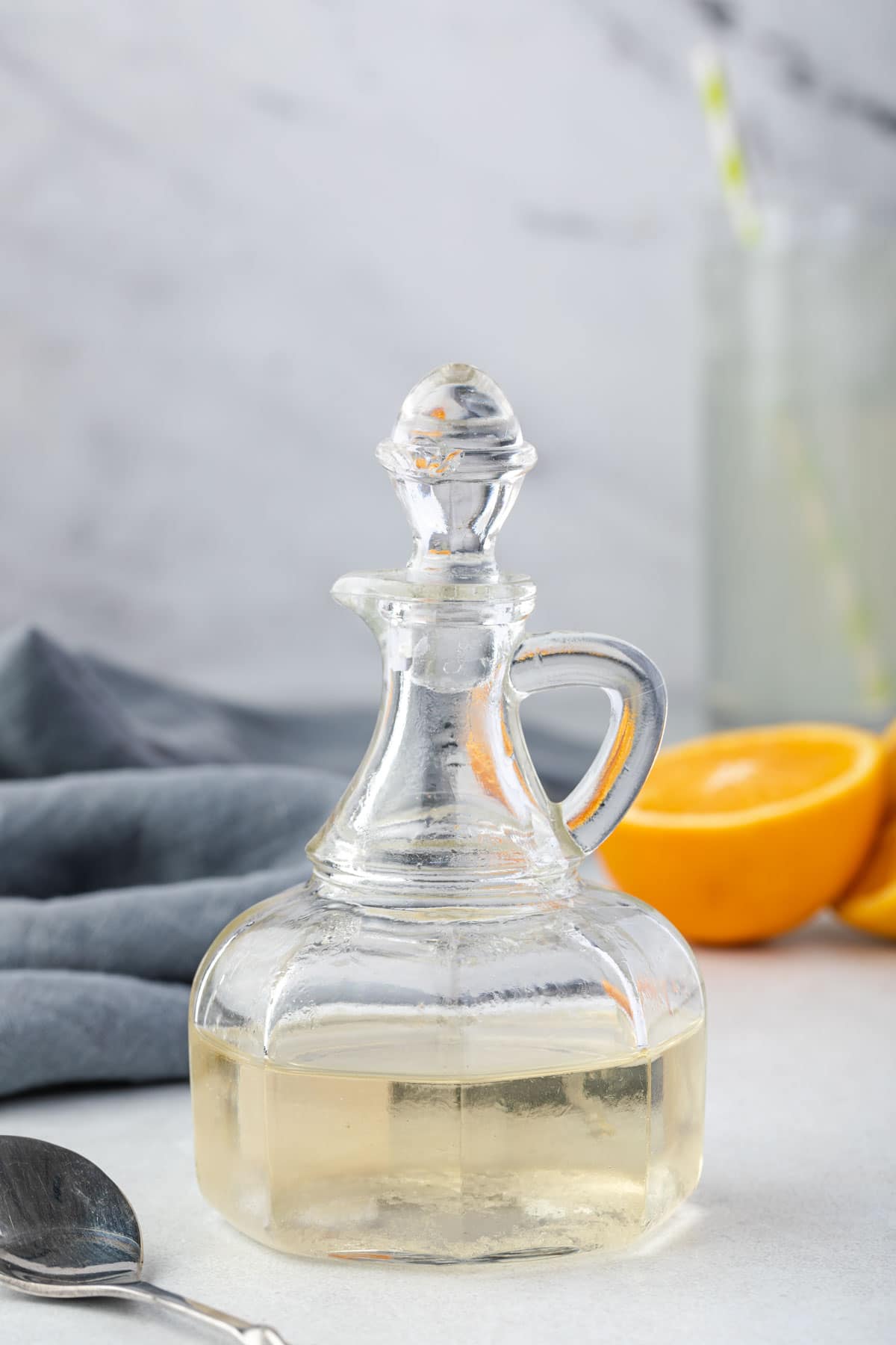 Simple syrup in a glass bottle with orange half and drink in background.