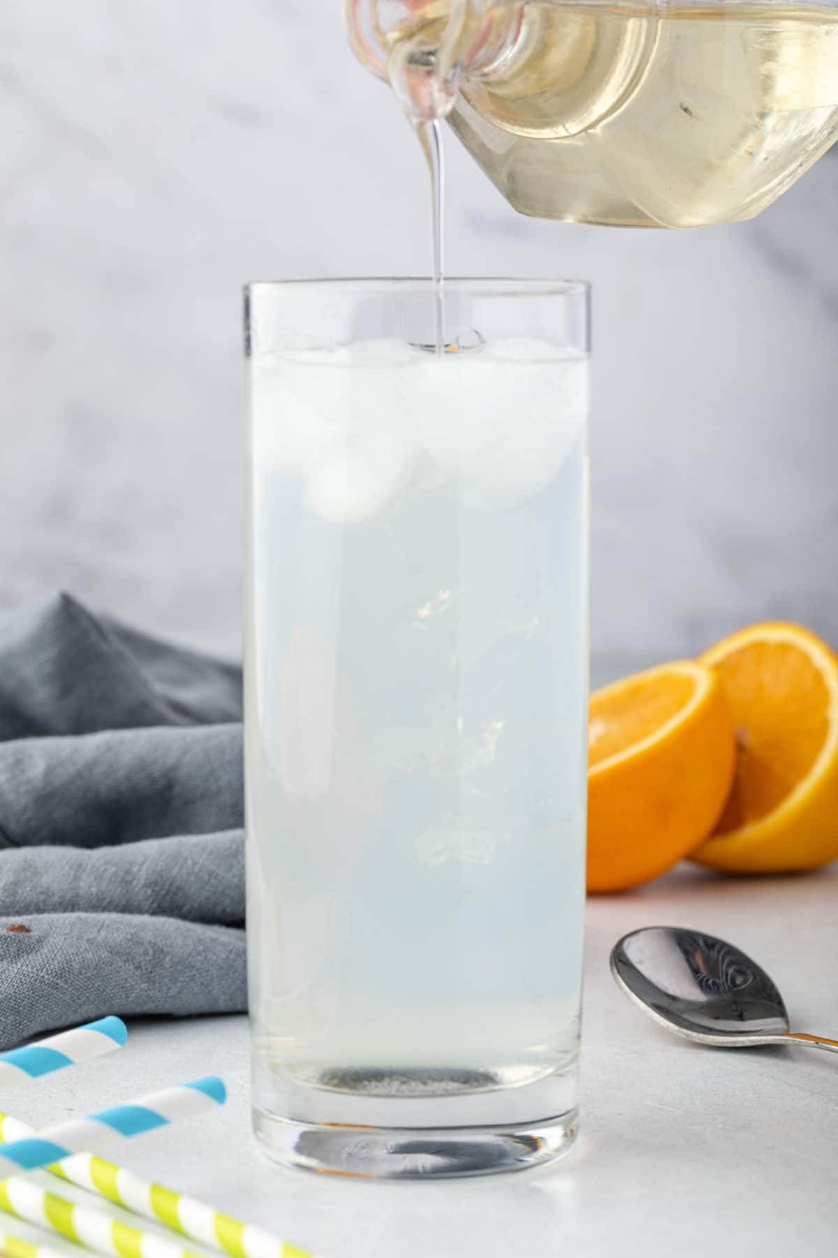 Pouring simple syrup into a tall glass filled with liquid and ice.