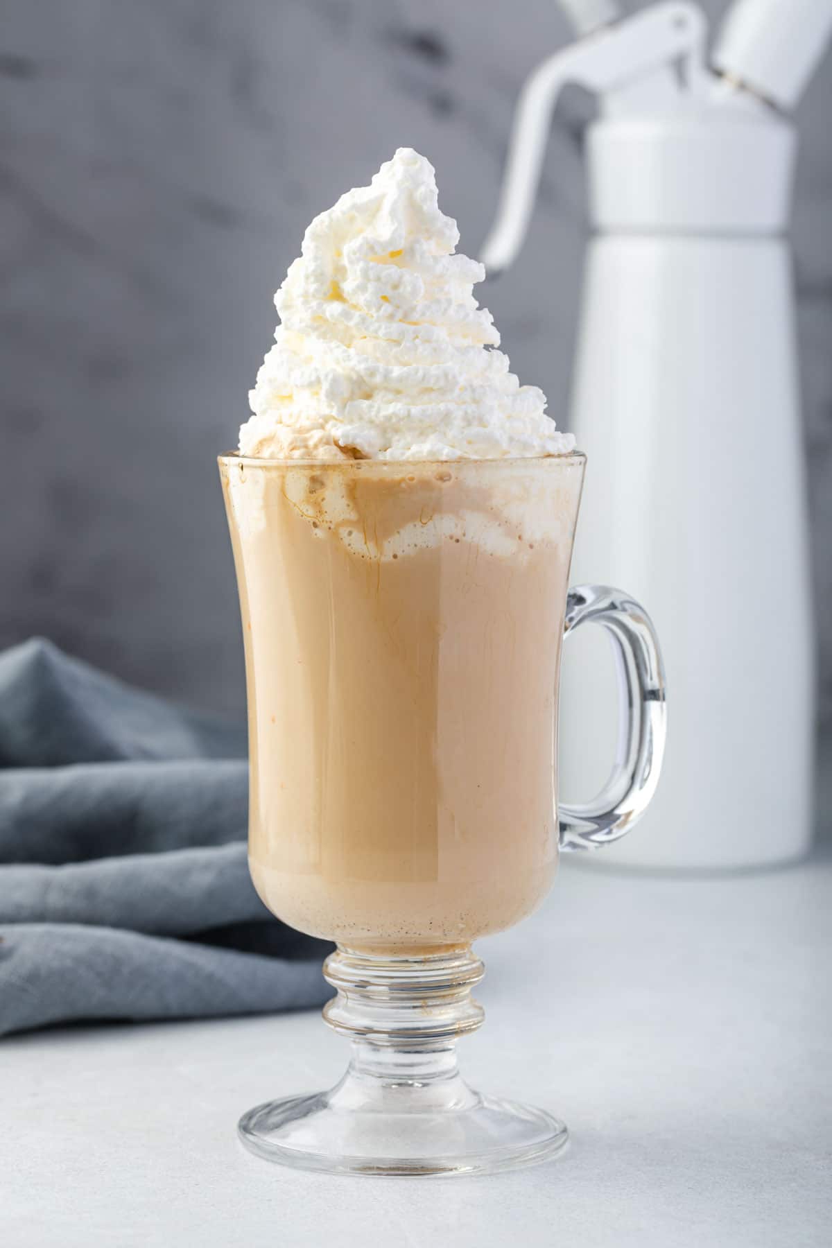 Iced coffee topped with whipped cream with dispenser in background.