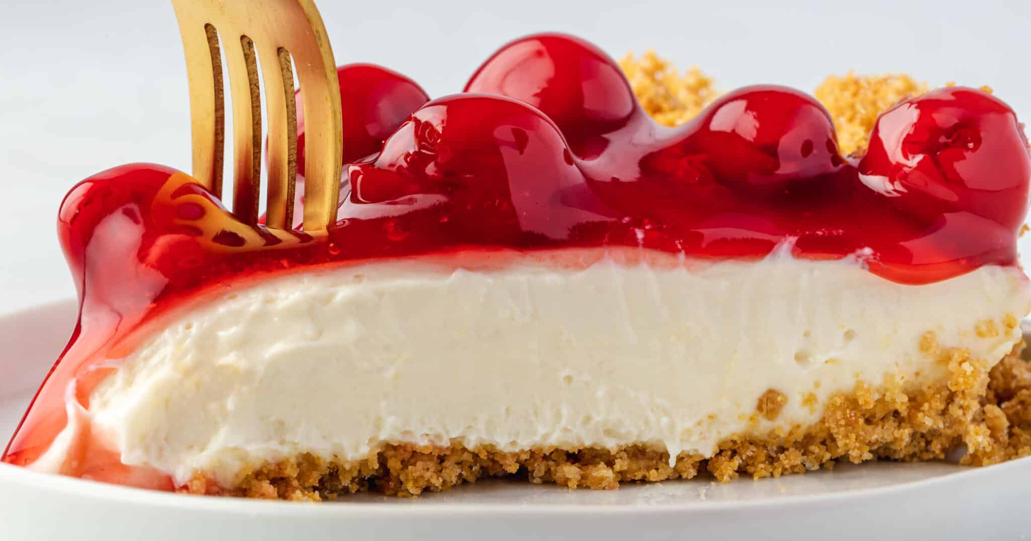 Gold fork sticking in to the front of a slice of cherry cream cheese pie.