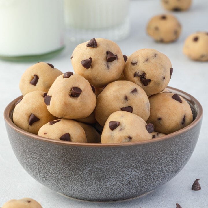Bowl of edible cookie dough balls with a glass of milk in background.