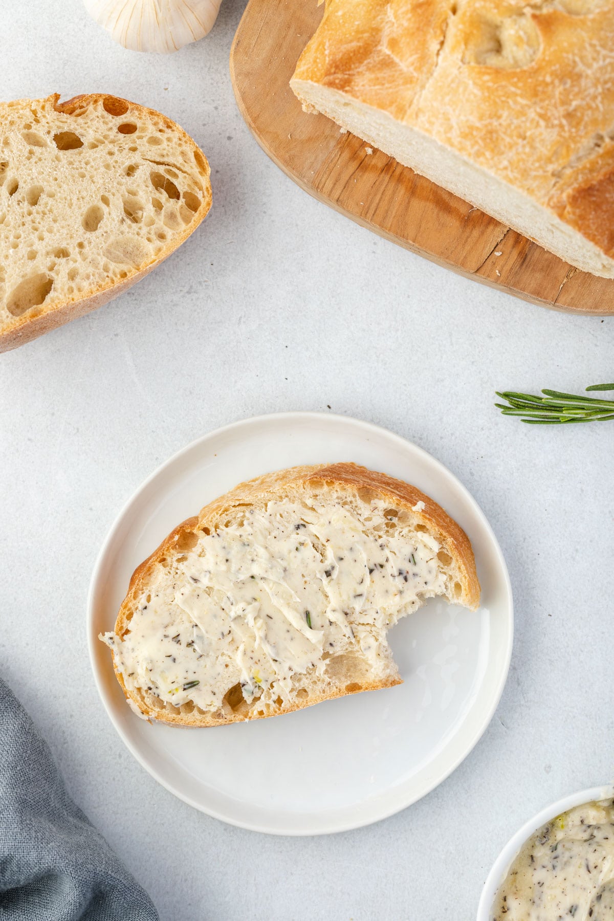 Bread topped with garlic rosemary butter on a plate, with bread on a board at top of image.