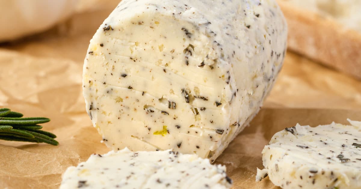 Rosemary butter in a log shape on parchment with 2 circles of butter sliced off.