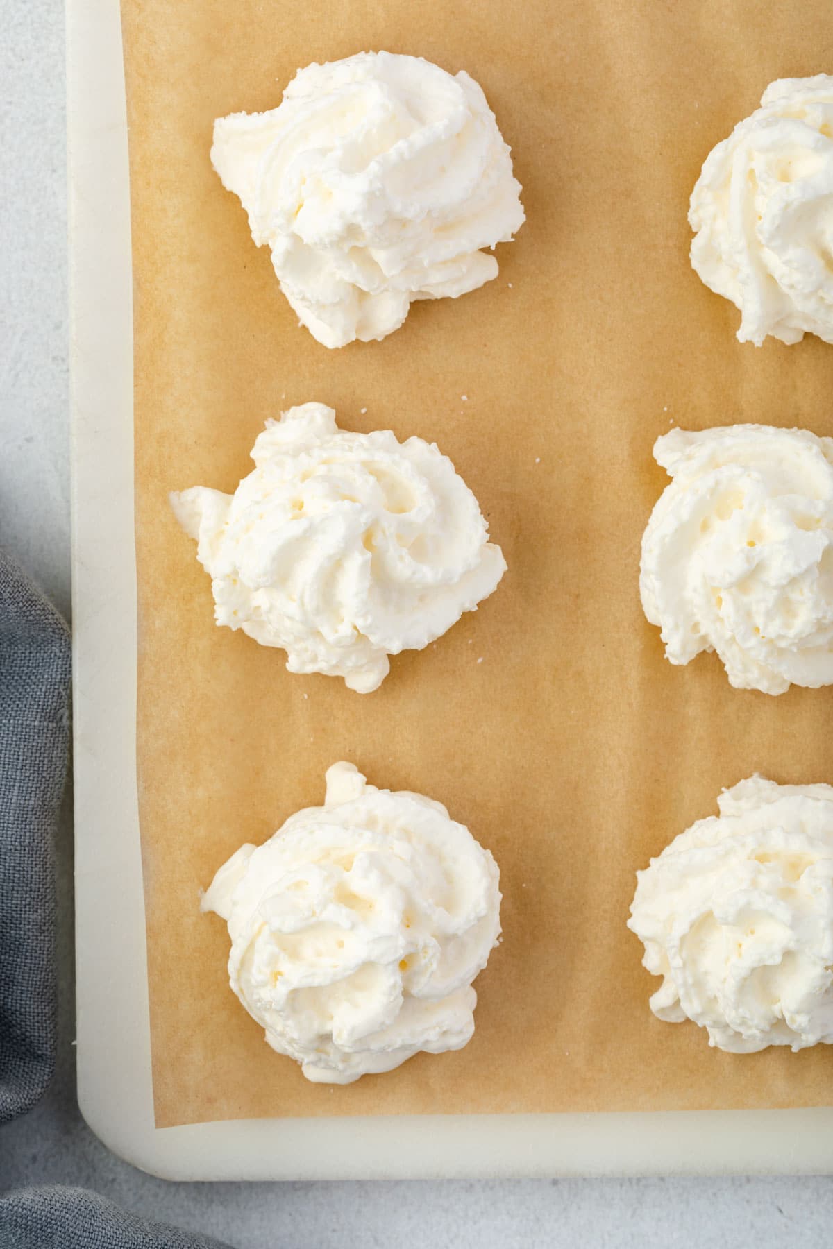 Whipped cream piped in a circles on a sheet of parchment.