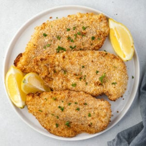 Platter of breaded chicken cutlets on a platter with lemon wedges.