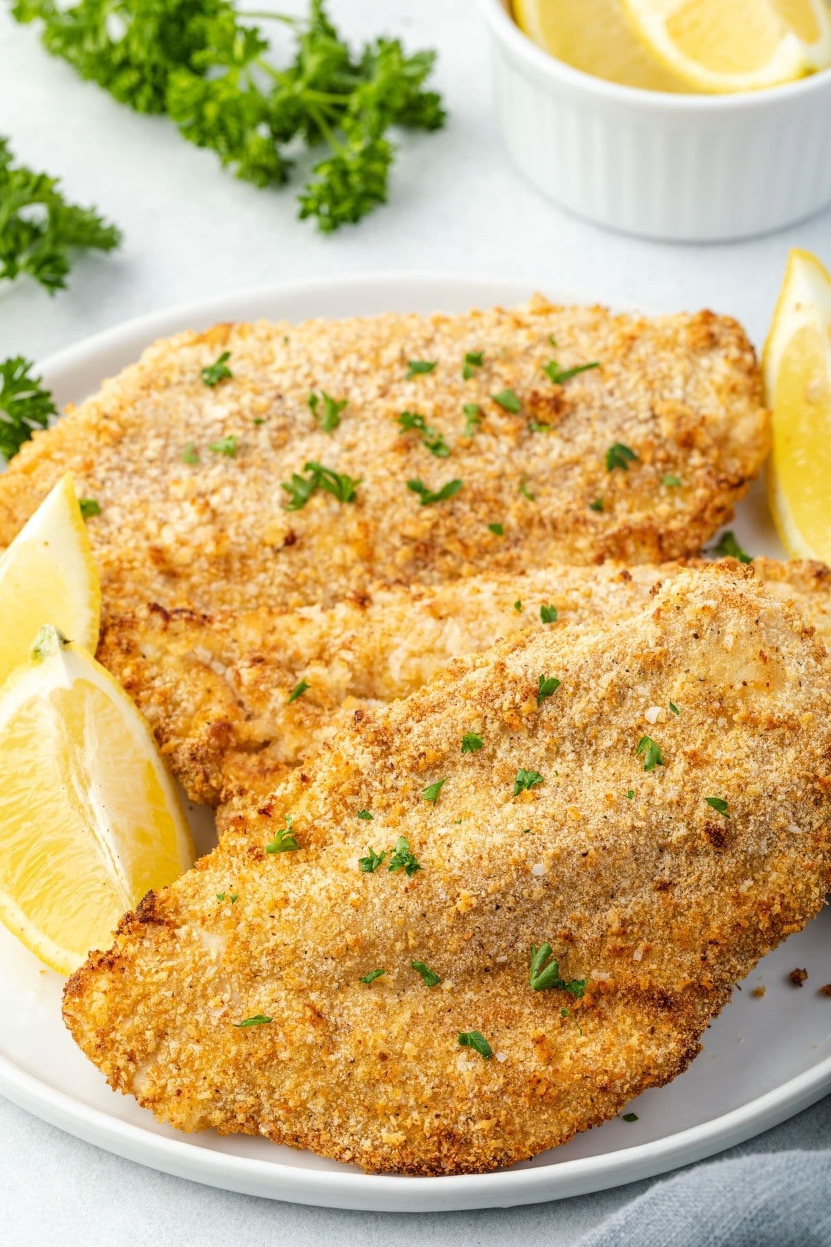 Platter of breaded chicken cutlets on a platter with lemon wedges.