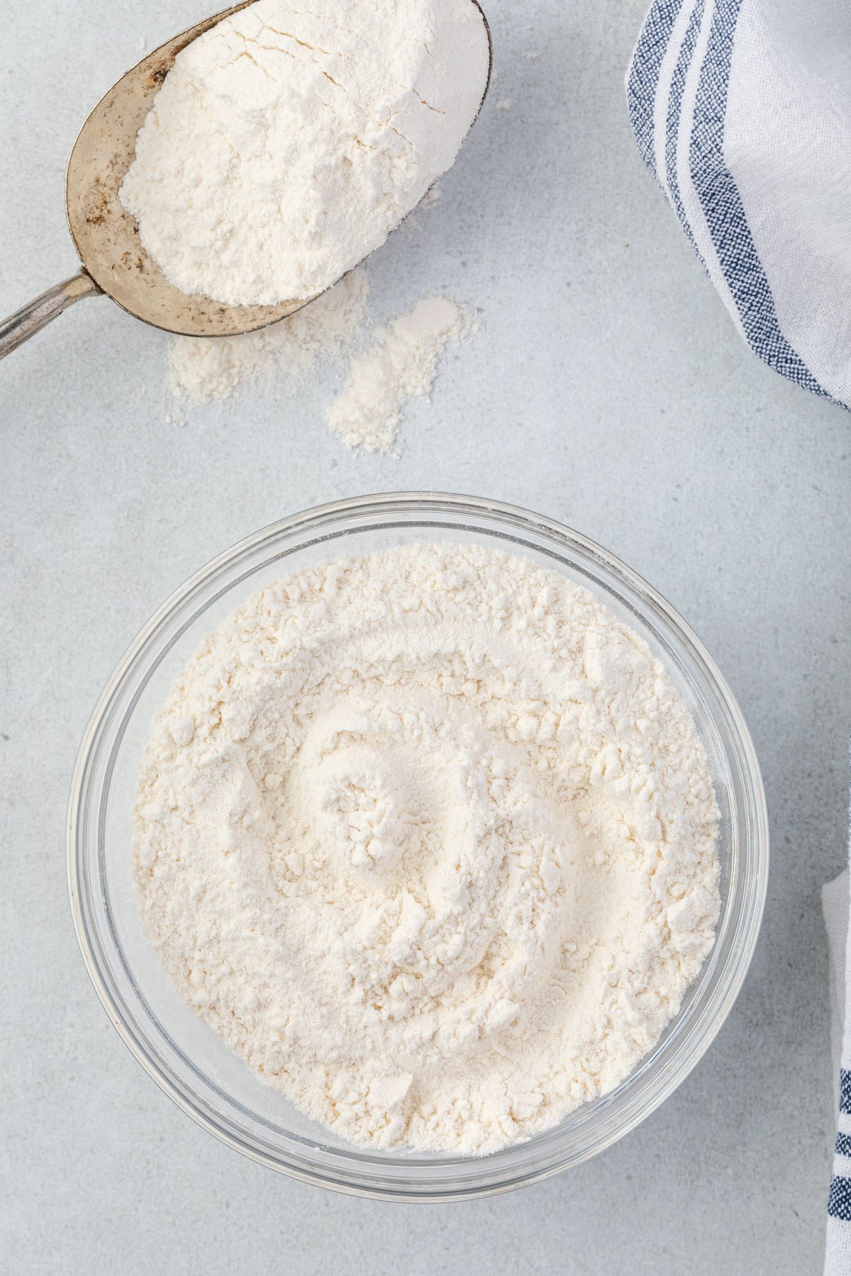 Flour in a bowl, and an antique scoop with flour spilling out of it.