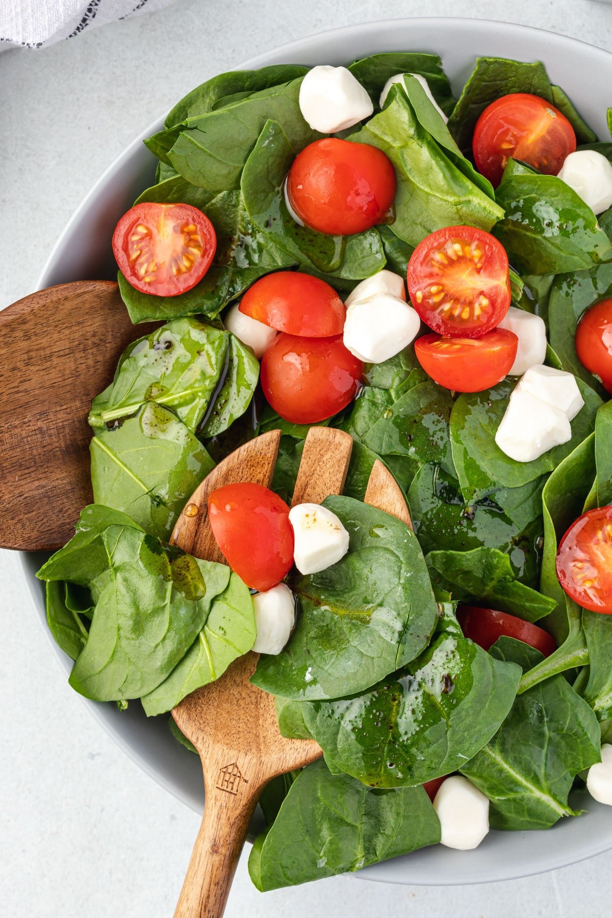 Spinach caprese salad being served with wooden salad servers.