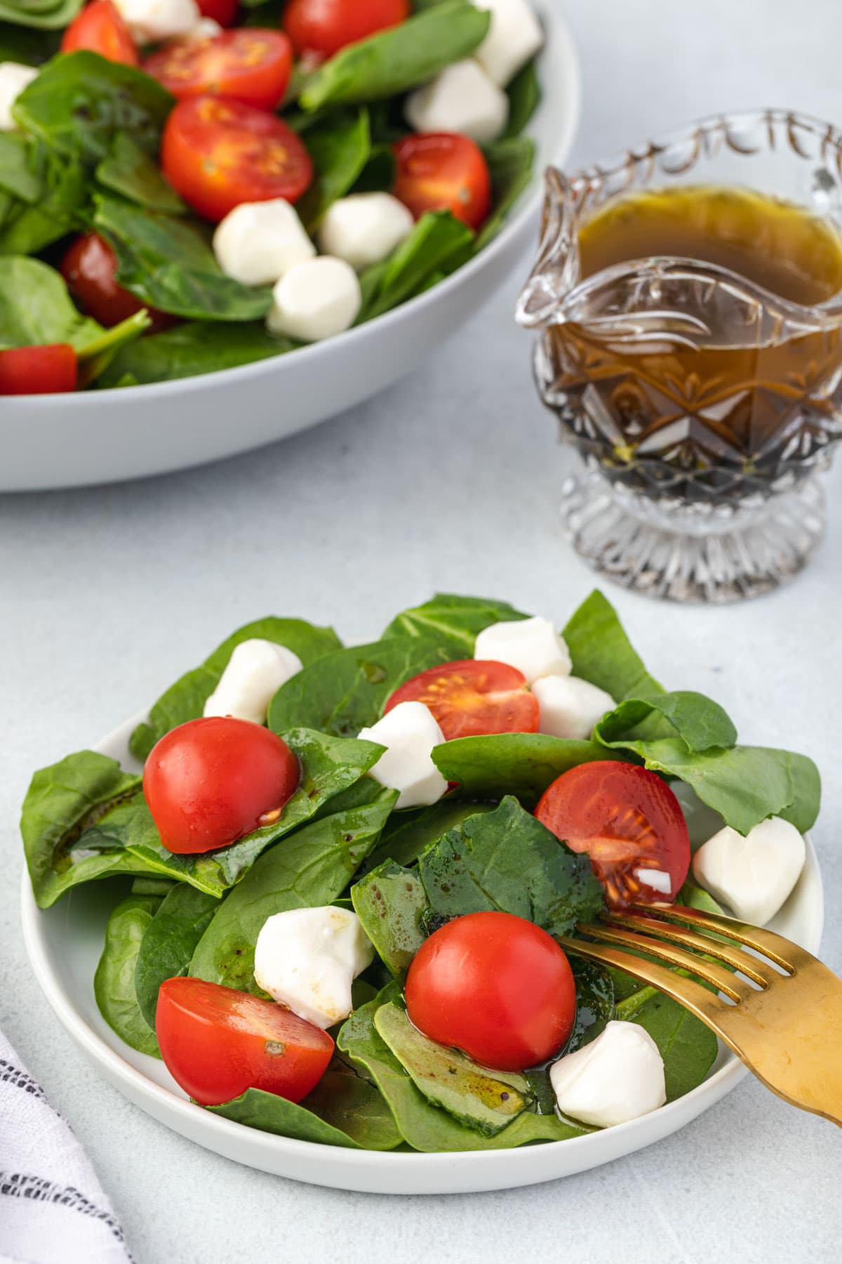Individual plate of spinach, cheese, and tomatoes, with crystal dressing pitcher.