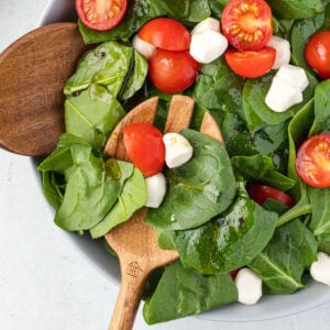 Spinach caprese salad being served with wooden salad servers.