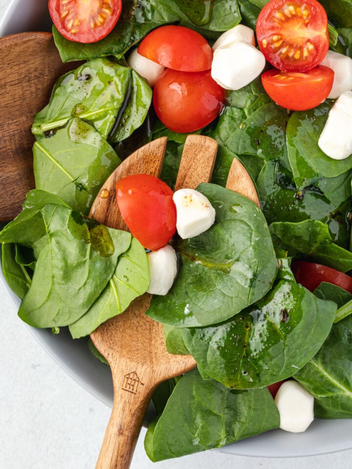 Spinach caprese salad being served with wooden salad servers.