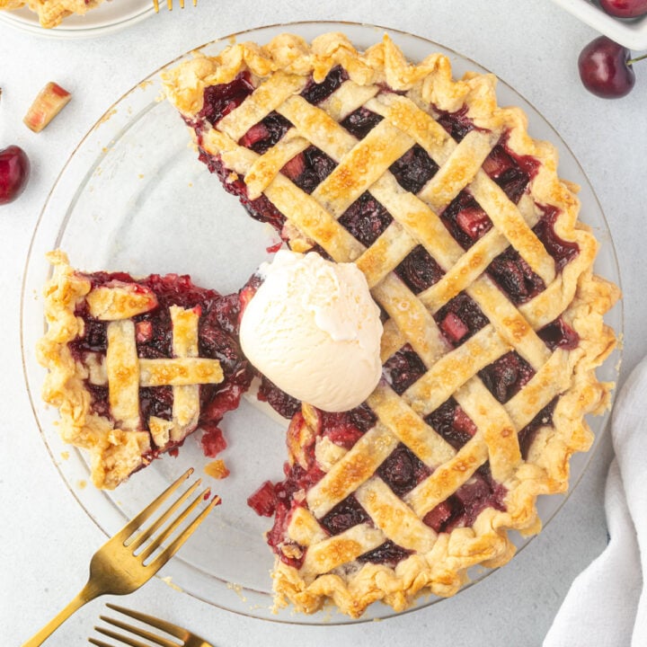 Overhead of a cherry rhubarb pie with pieces cut from it and a scoop of ice cream on the top of the pie.