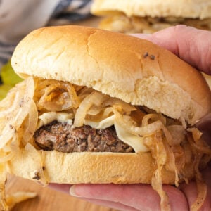 Close up of a hand holding a cheeseburger piled with caramelized onions.
