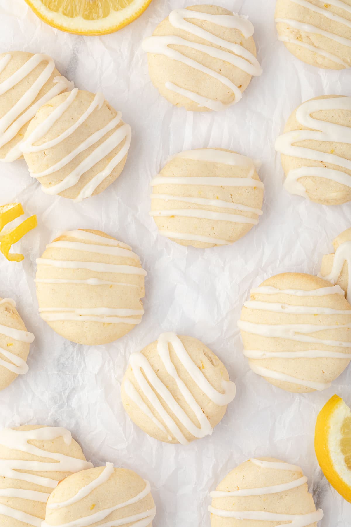 Overhead of small lemon butter cookies on white parchment with frosting drizzled on cookies.