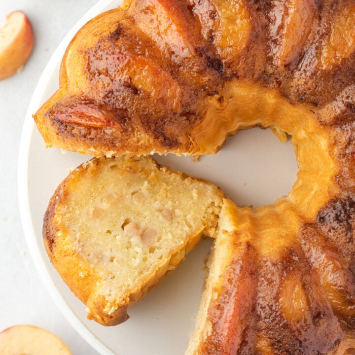 Peach bundt cake with a slice cut and laying on cake plate.