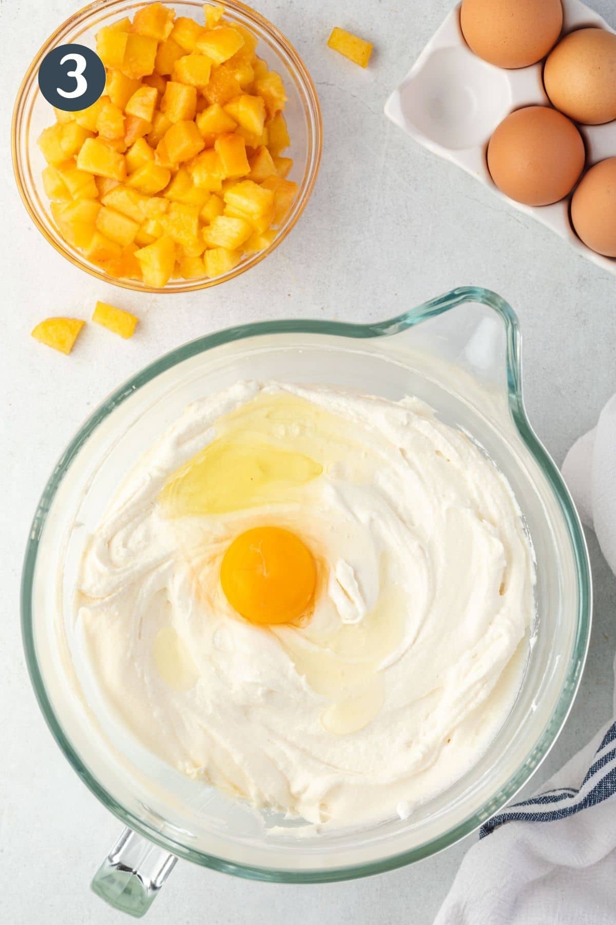 Egg on top of batter in large bowl with chopped peaches in a bowl.