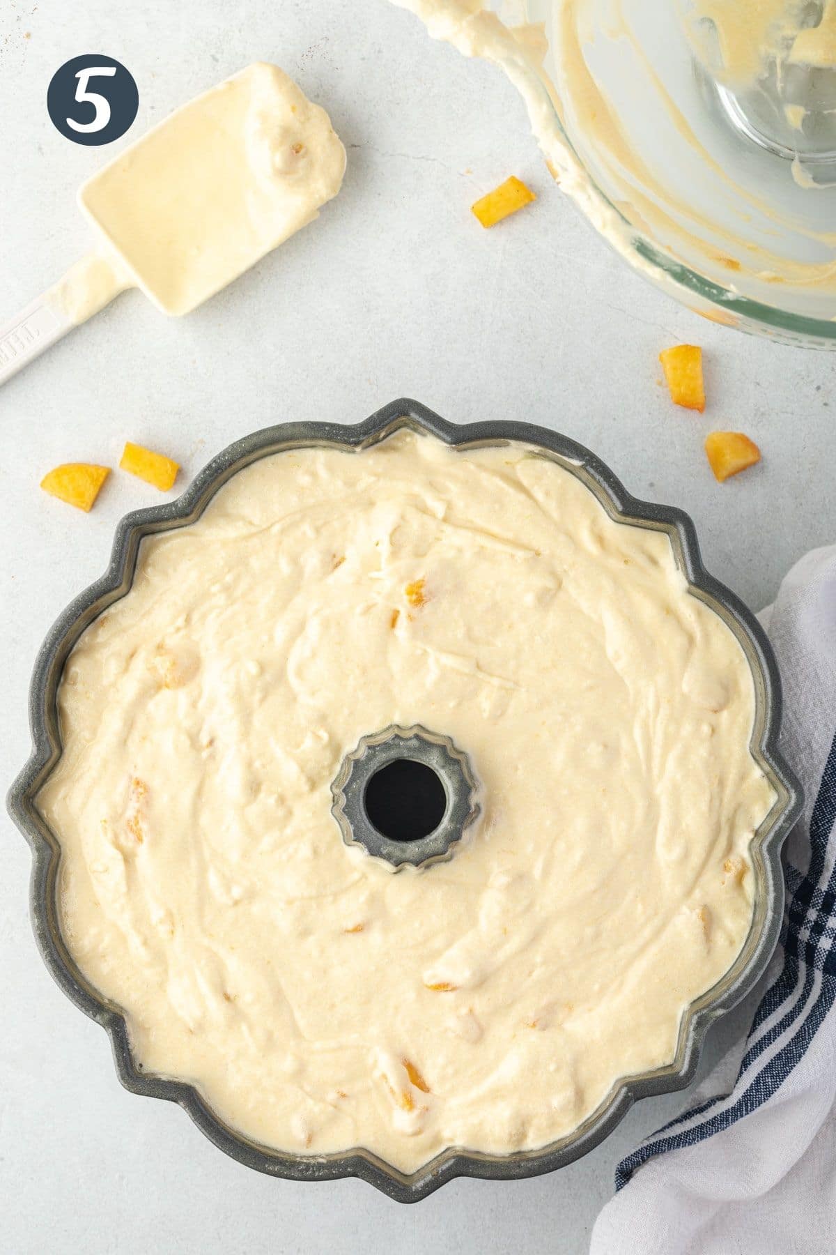 Pound cake batter filling bundt pan with chopped peaches sprinkled around.