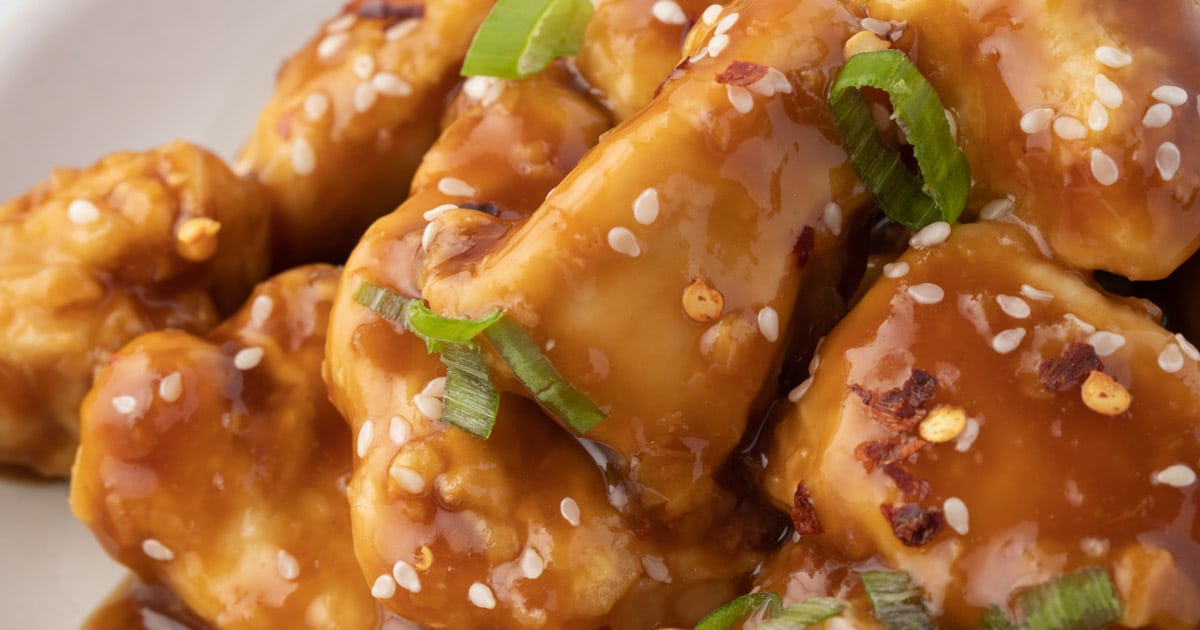 Close of of teriyaki chicken pieces, with sesame seeds and green onion.