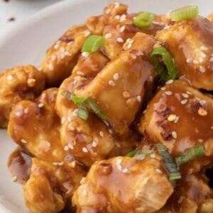 Close of of teriyaki chicken pieces, with sesame seeds and green onion.