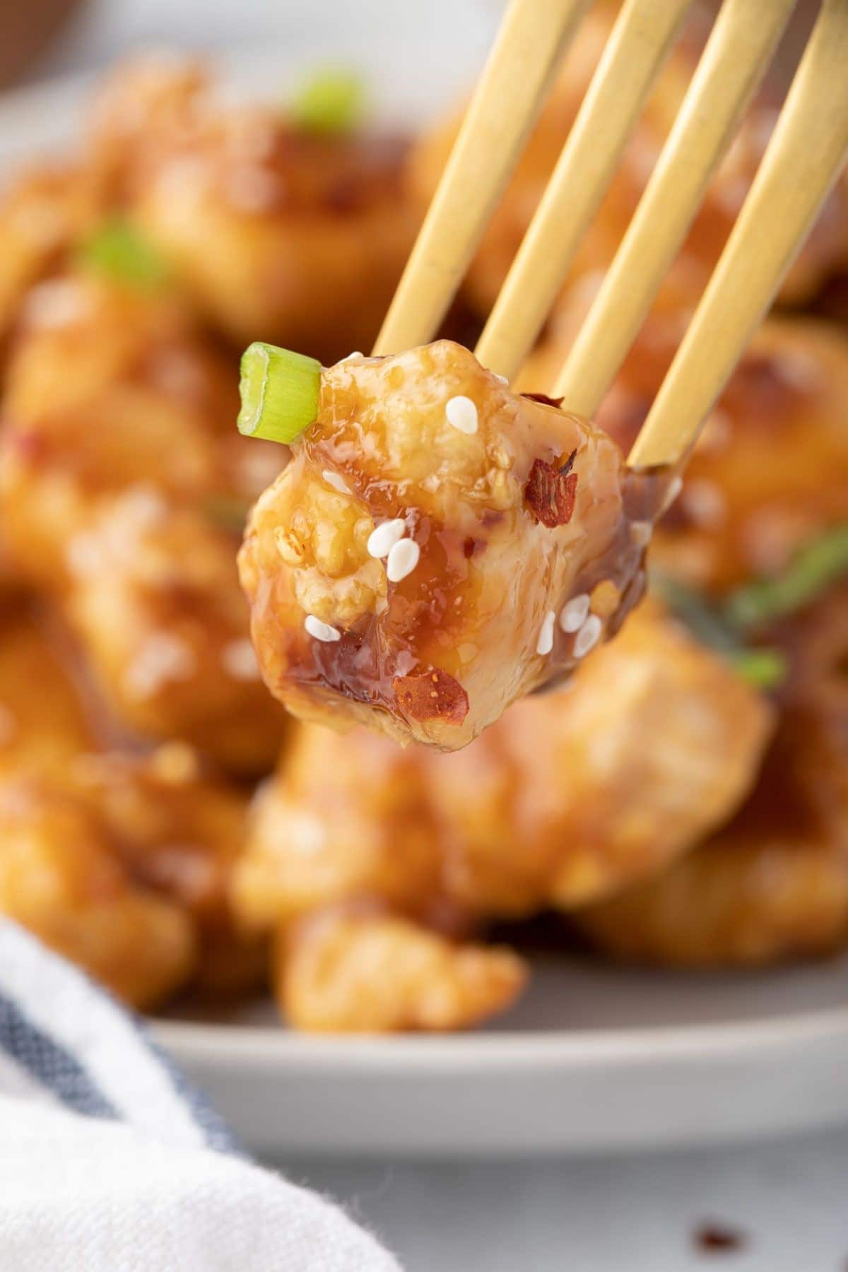 Close up of a piece of teriyaki chicken on a gold fork.