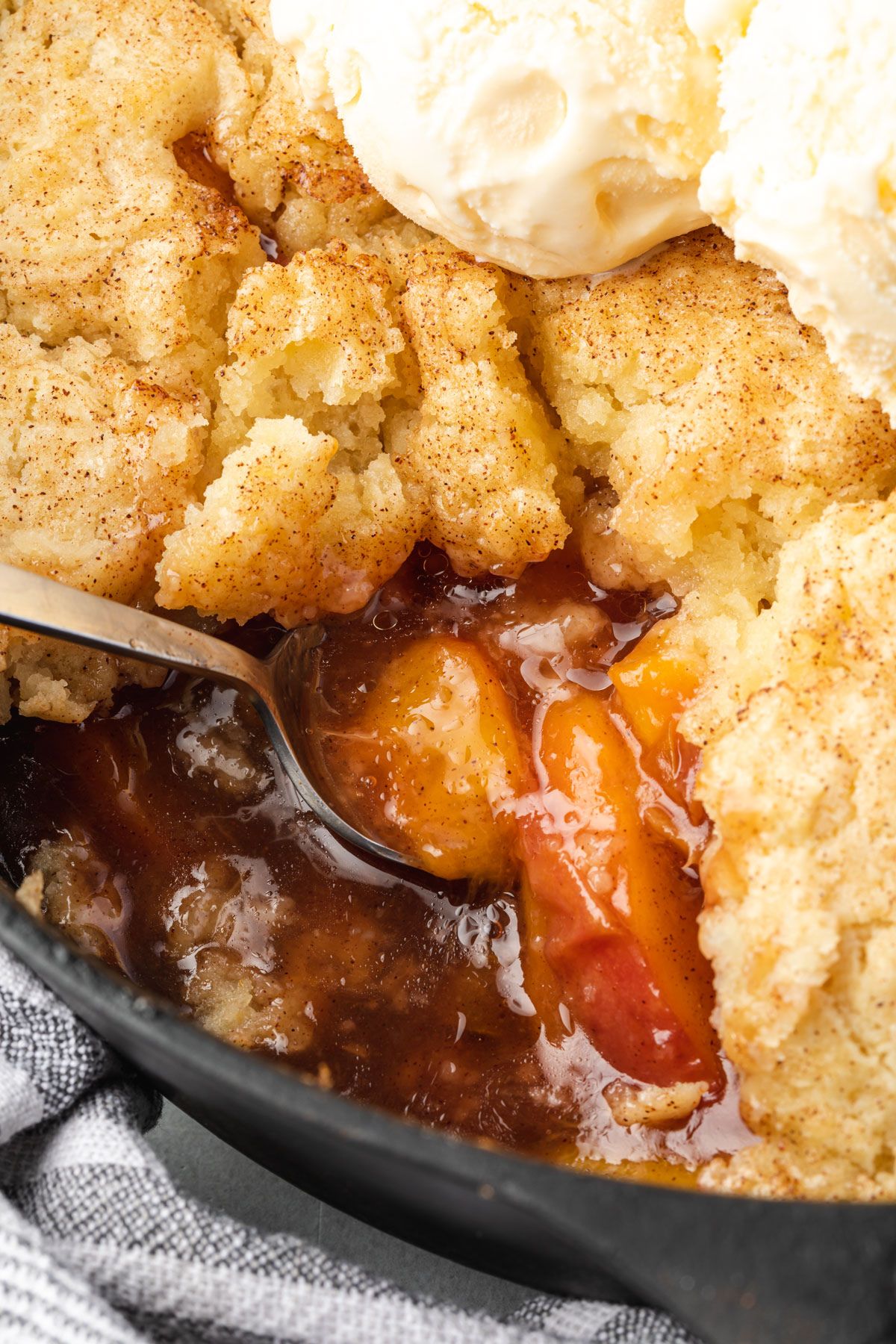 Close up of cobbler where a serving was scooped out, showing gooey peach filling.