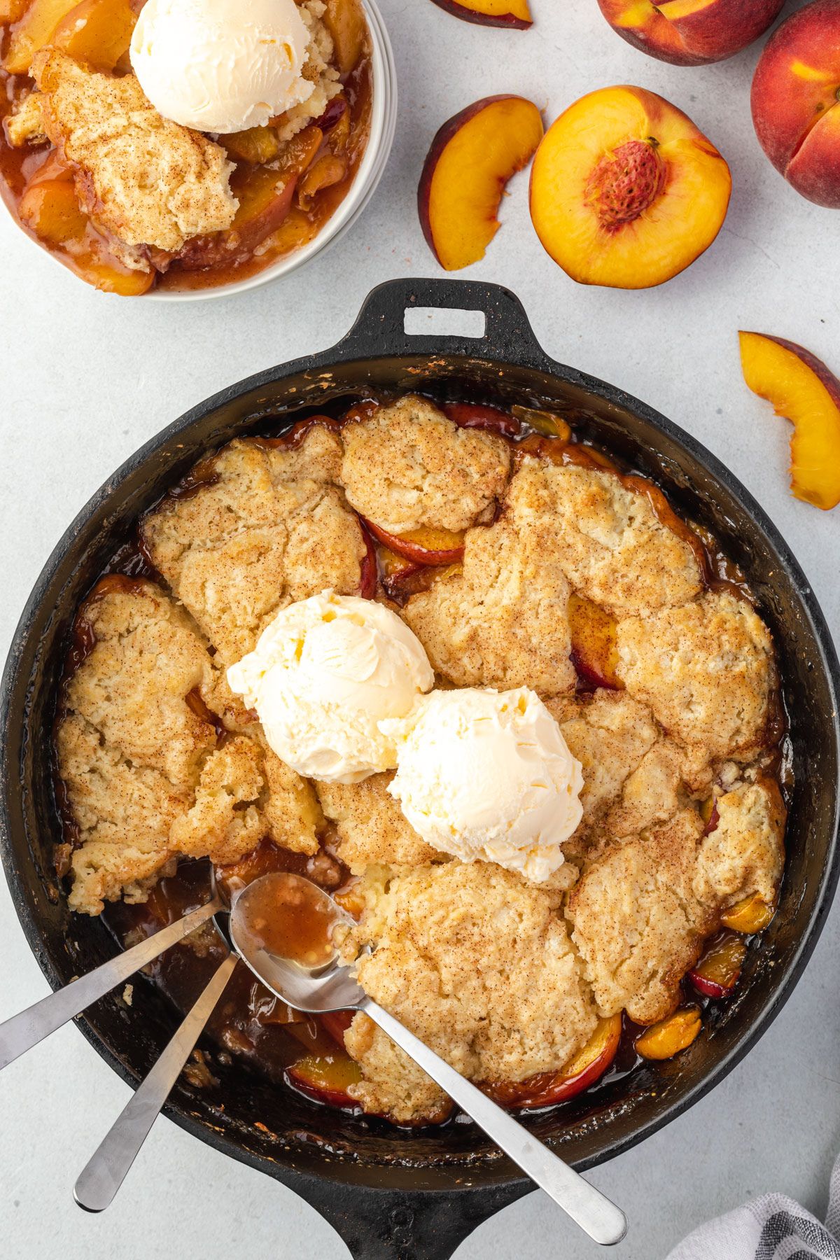 Cobbler in a cast iron skillet with 3 spoons where one portion of cobbler was.