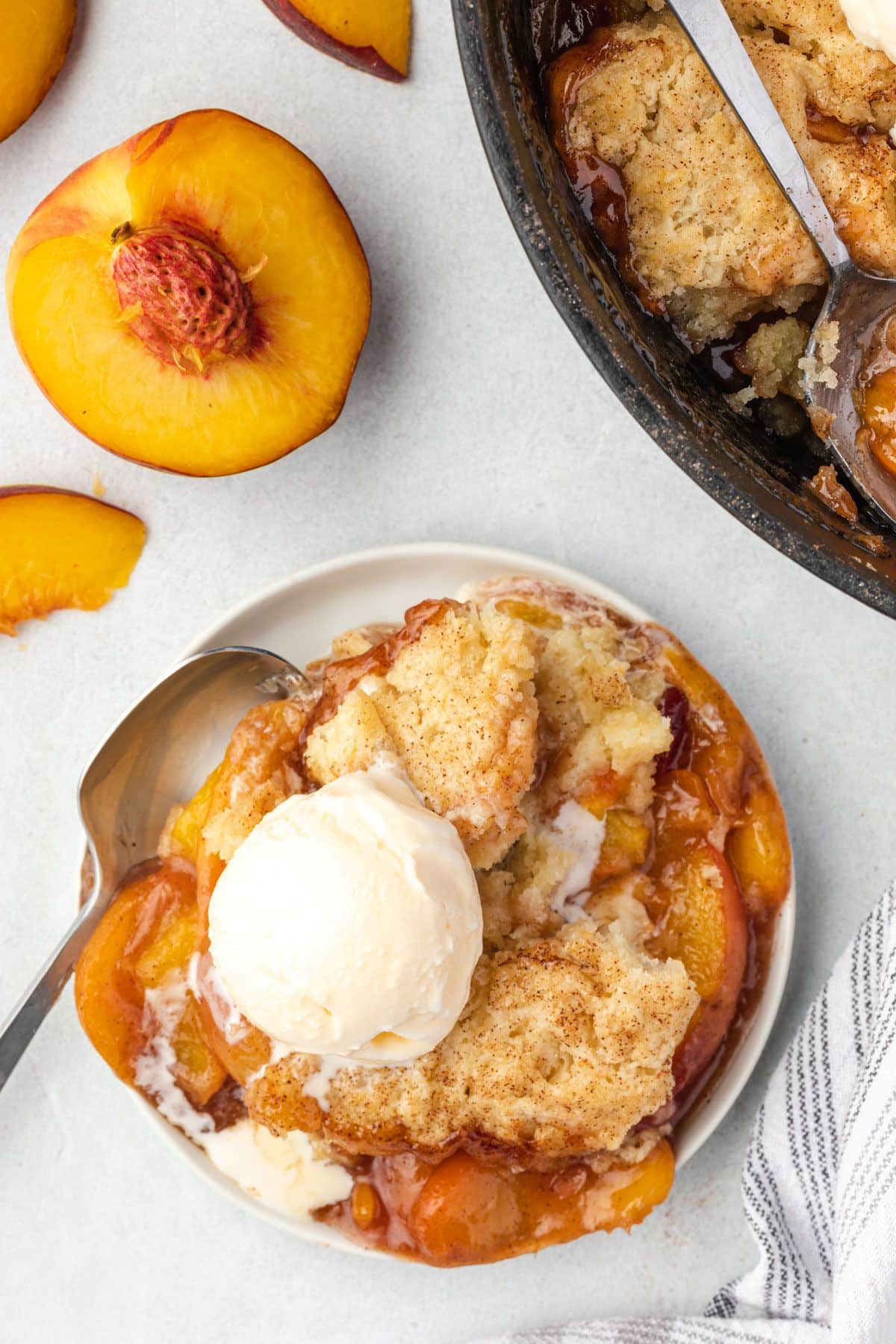 Peach cobbler served on a white plate with a scoop of ice cream on top.