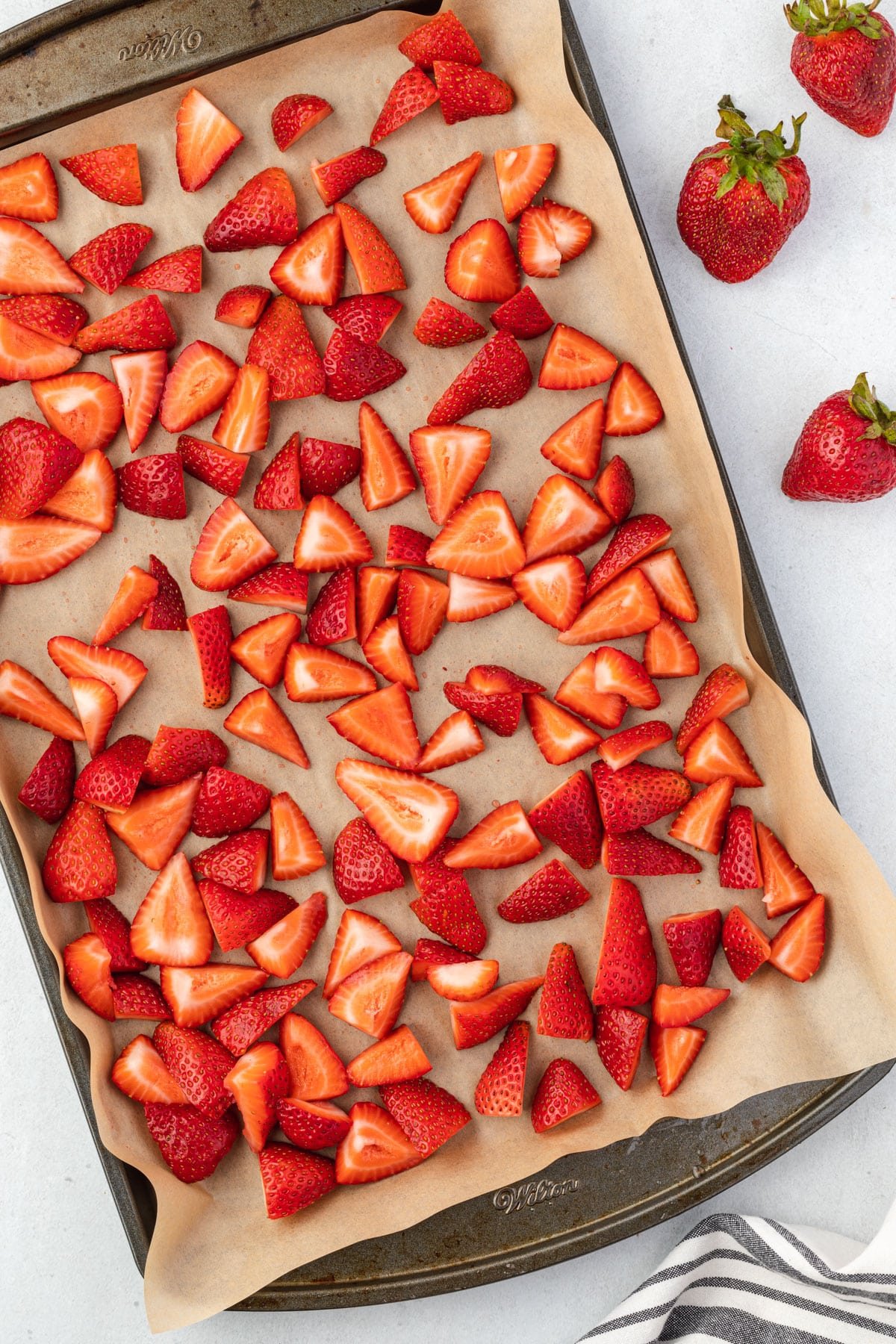 Overhead of cut strawberries on a parchment lined baking sheet.