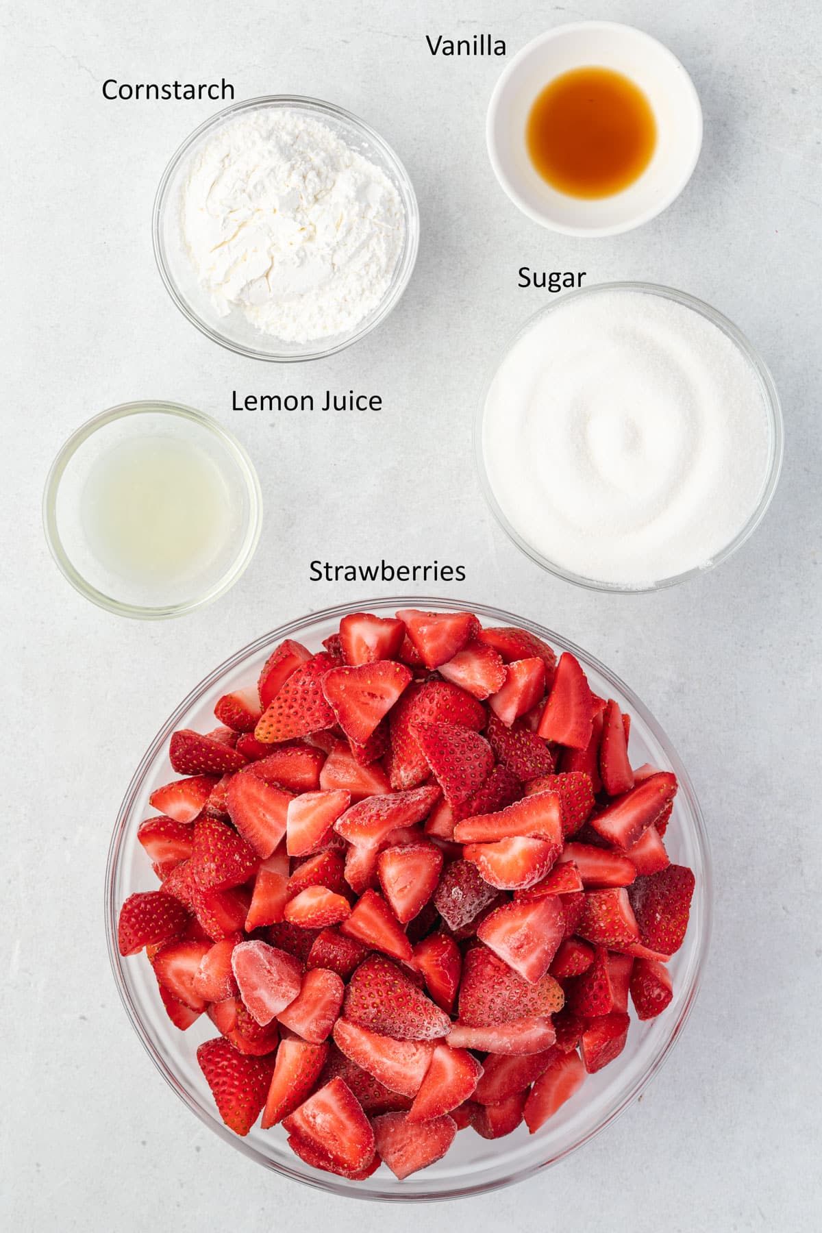 Overhead labeled ingredients for filling: Frozen strawberries, sugar, lemon juice, cornstarch, and vanilla.