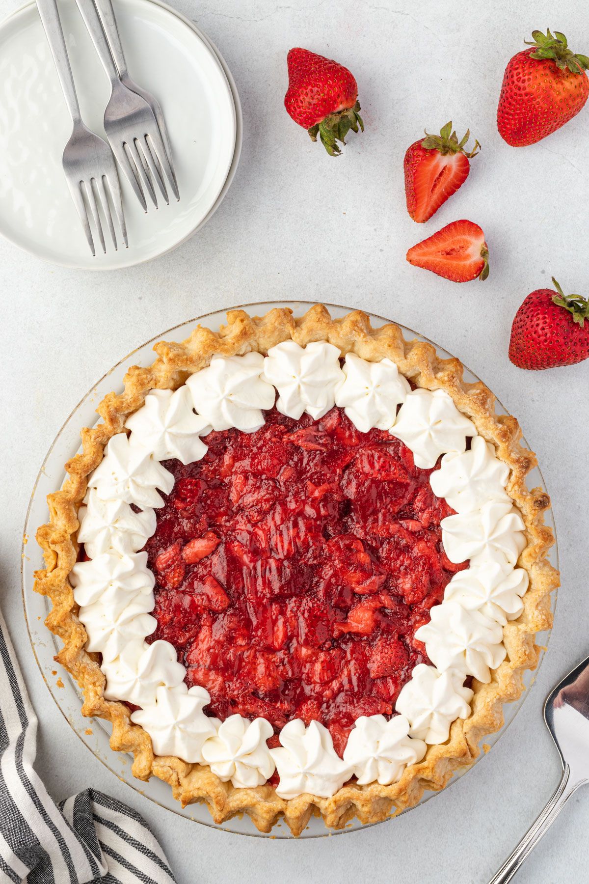 Overhead of an uncut strawberry pie made with frozen strawberries and topped with dollops of whipped cream.