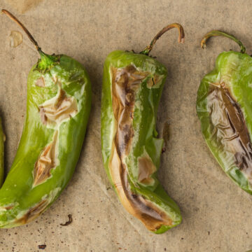 4 charred hatch chiles on brown parchment.