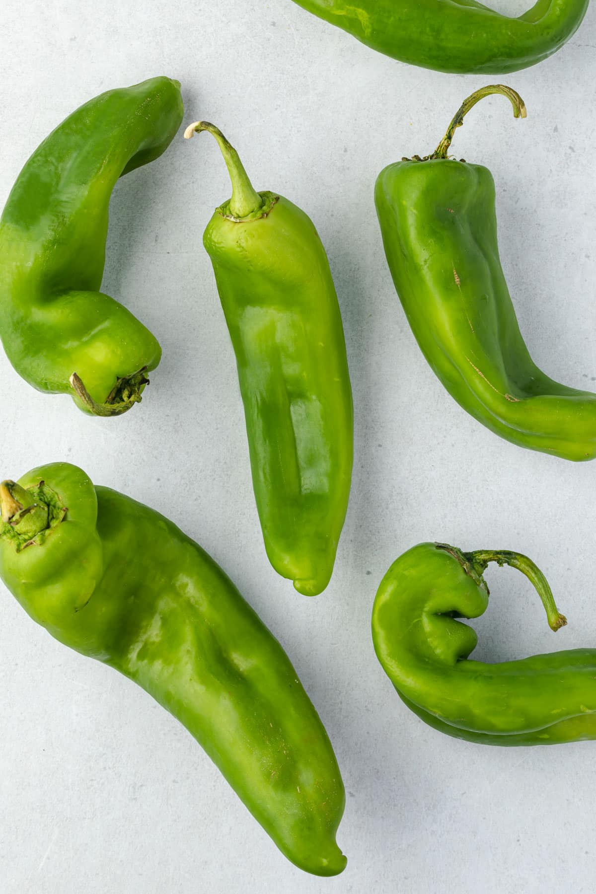 6 bright green hatch chiles scattered on a cement backdrop.