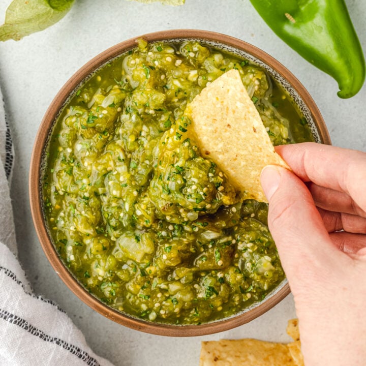 Hatch chile salsa verde in a bowl, with a hand dipping a chip into the salsa.
