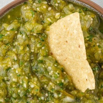 Bowl of green chile salsa verde with a chip in it.