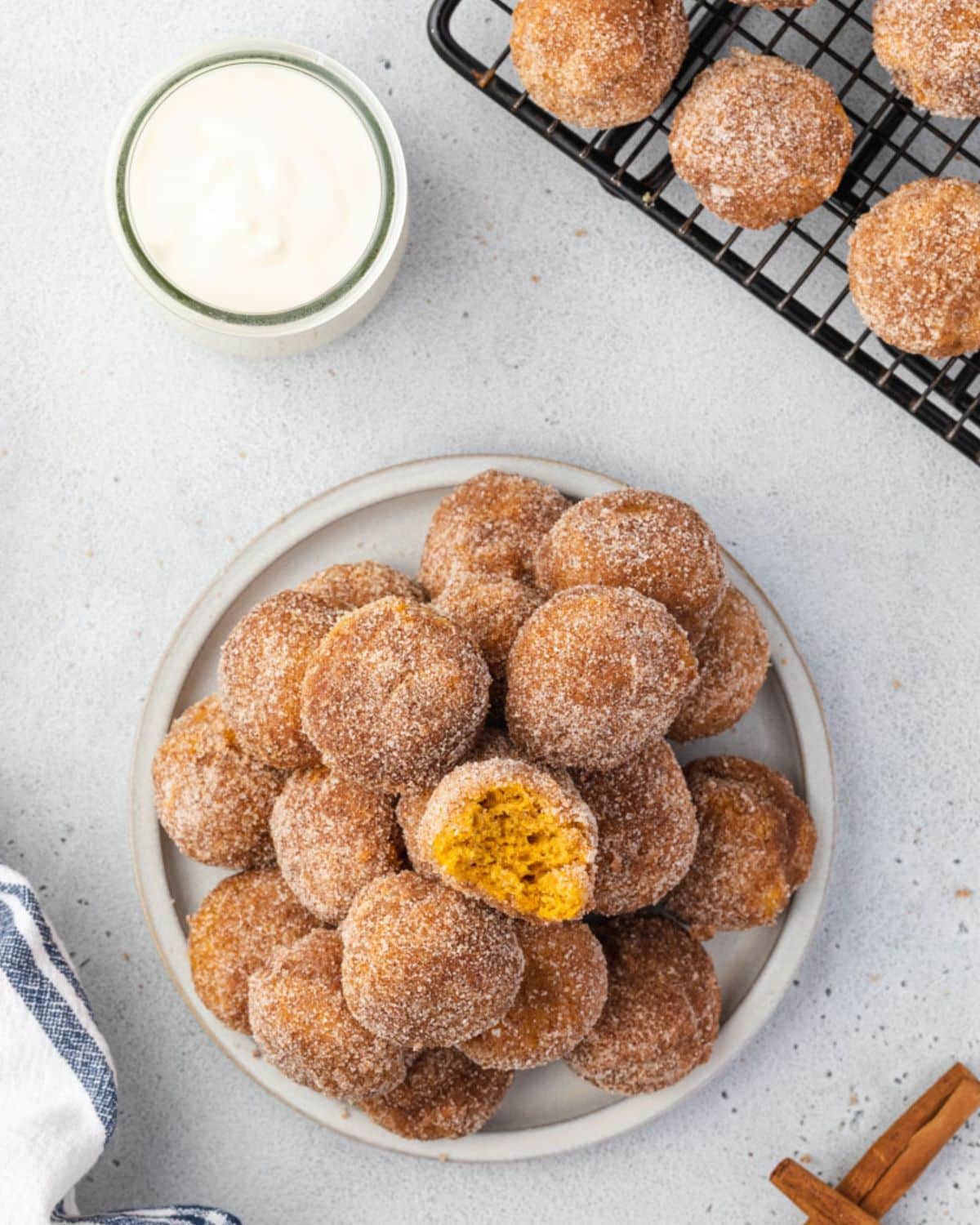 Overhead of donut holes on a plate, with a jar of cream cheese dipping sauce and more donut holes on a baking sheet.