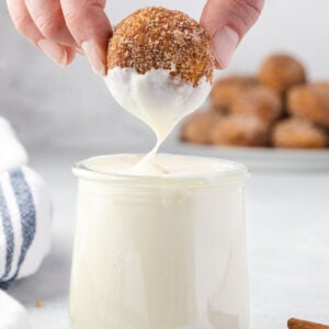Close up of a donut hole being dipped into the sweet cream cheese sauce.