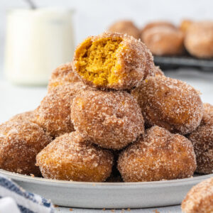 A stack of pumpkin donut holes on a plate, the one on the top has a bite out of it.