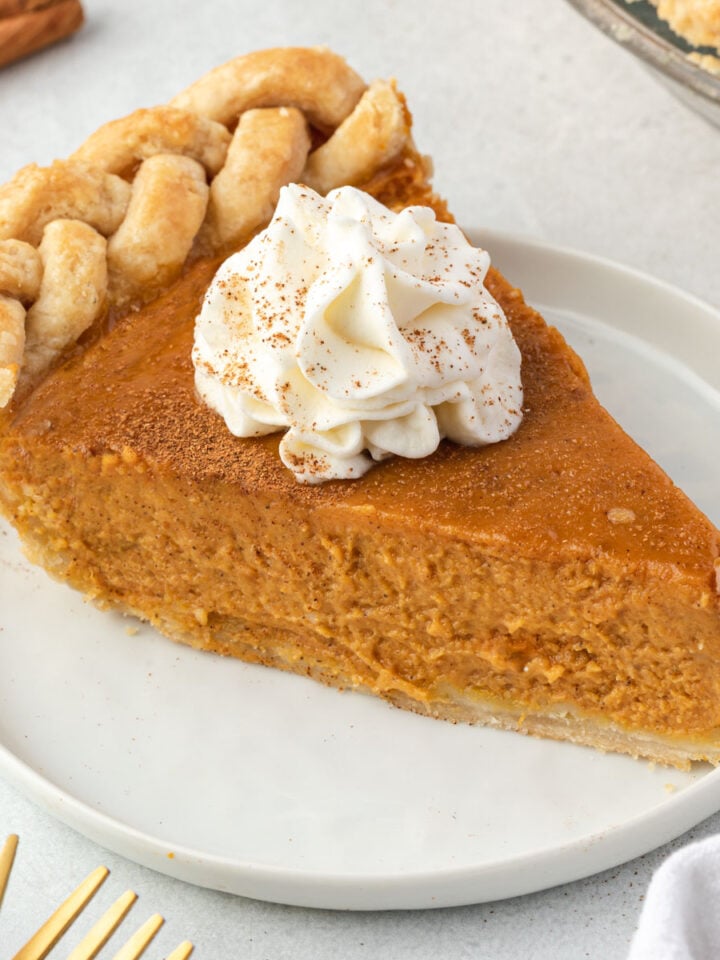 Close up of a slice of pumpkin pie with a dollop of whipped cream.