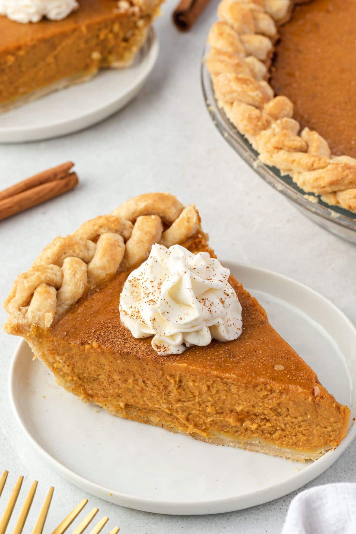 Slice of pumpkin pie on a plate, with the pie in 1 corner and another slice in the ohter.