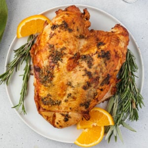 Roasted turkey breast on a plate with sprigs of rosemary and orange slices.