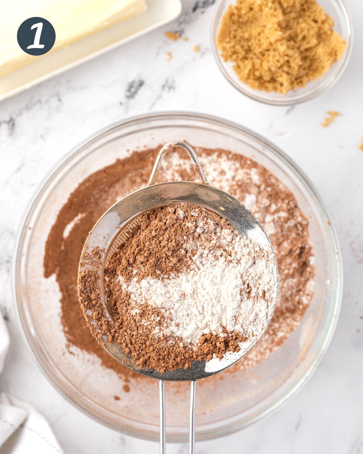 Cocoa powder and flour in a sifter over a bowl.