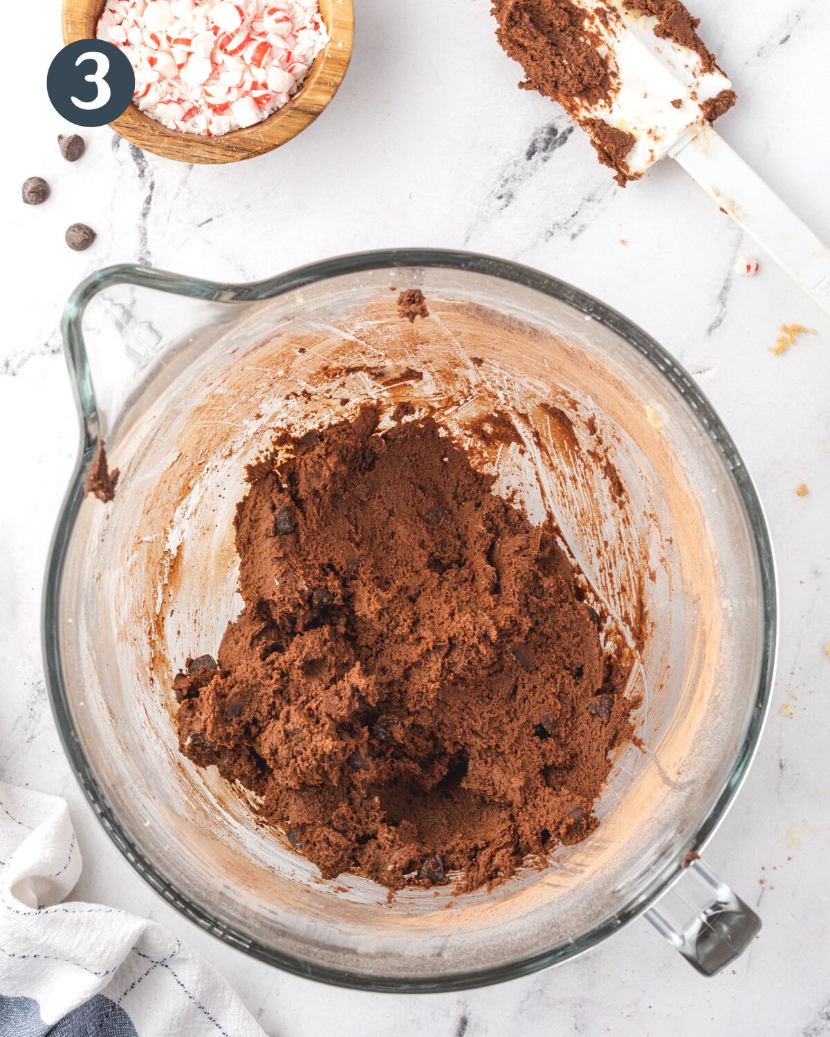 Thick chocolate batter in a large mixing bowl with a bowl of crushed peppermints by it.