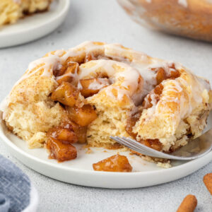 Close up of a cinnamon roll on a plate with apple pie filling spilling out of it.