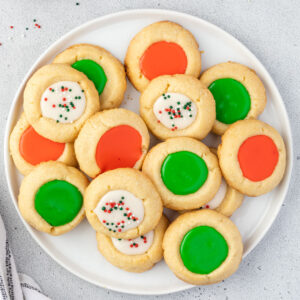 Overhead of a plate of assorted red, green, and white with sprinkles thumbprint cookies with icing.