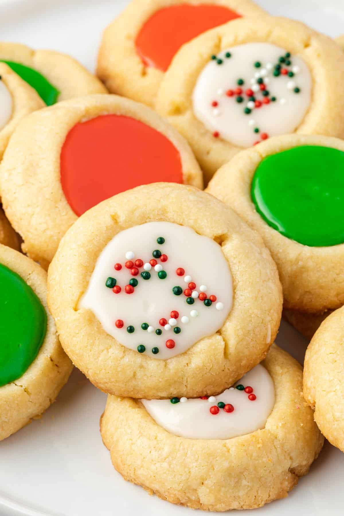 Stack of assorted (red, green, white with sprinkles) iced thumbprint cookies on a plate,