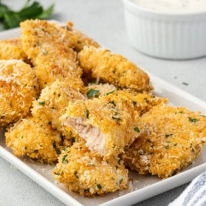 A pile of boneless parmesan garlic wings on a rectangular platter, chicken in center has a bite out of it.