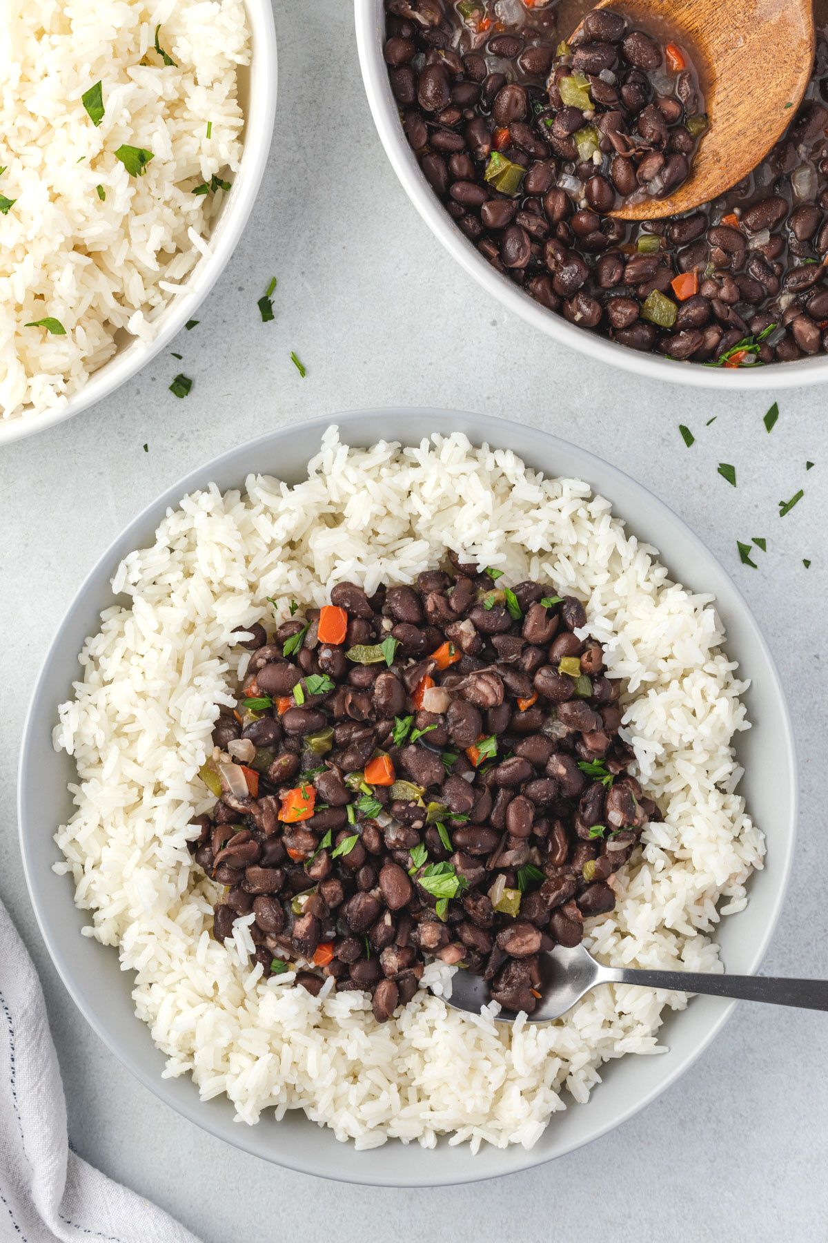 Bowl of quick cuban black beans over a bed of rice, serving bowls of rice and beans in top corners.