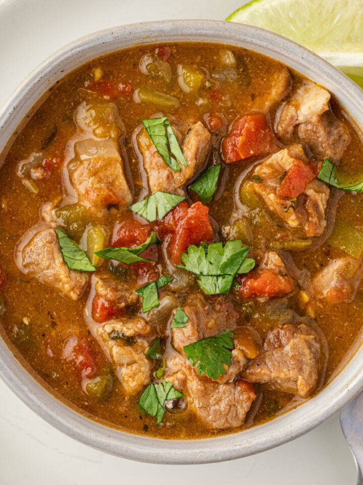 Bowl of pork green chili garnished with cilantro and a lime wedge.