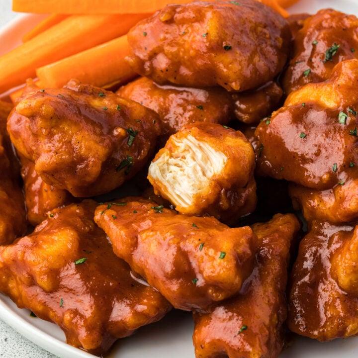 Close up of a plate of bbq chicken wings, one piece of chicken has a bite out of it.
