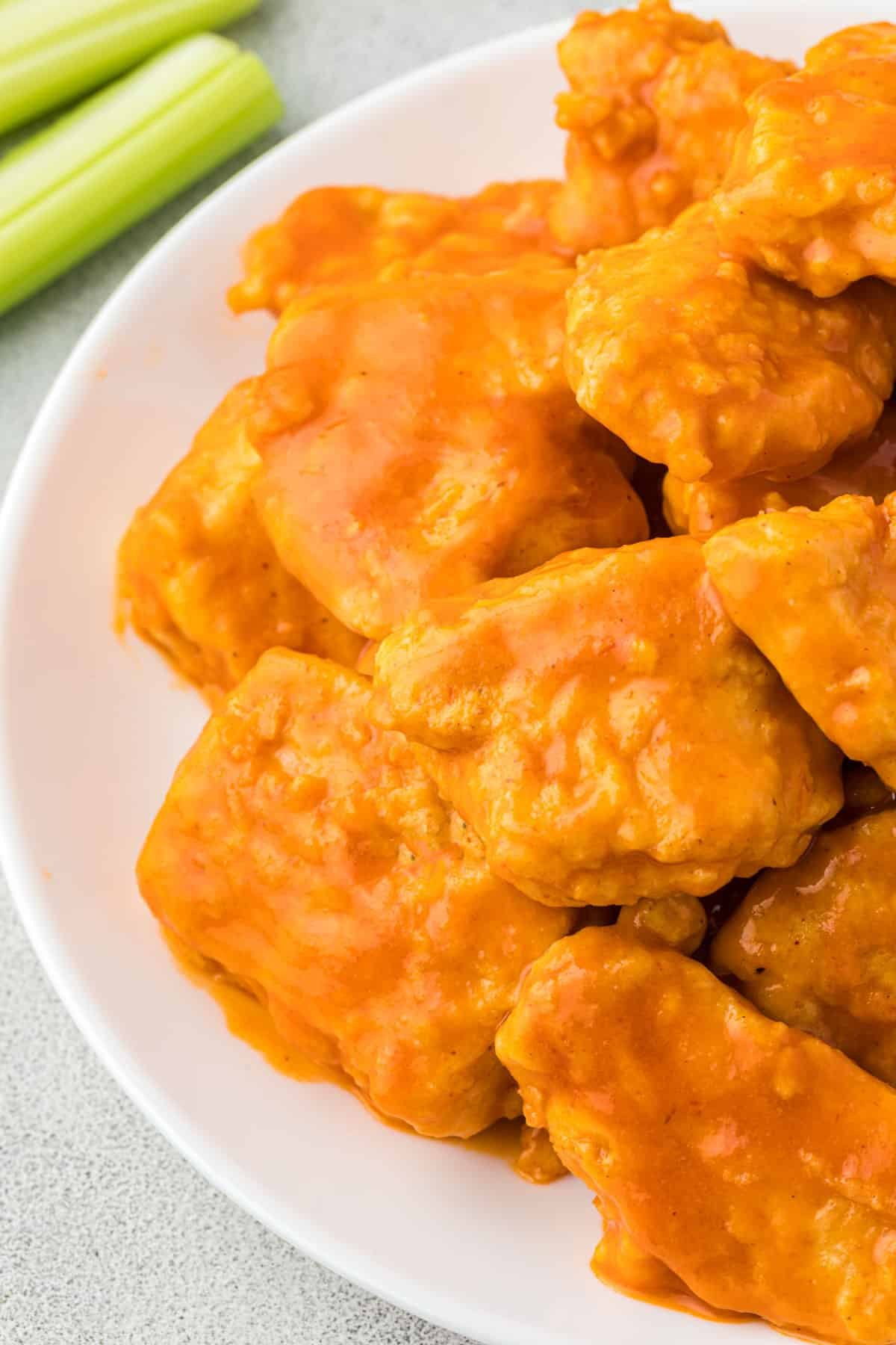 Half of a white plate with a close up of buffalo chicken bites.